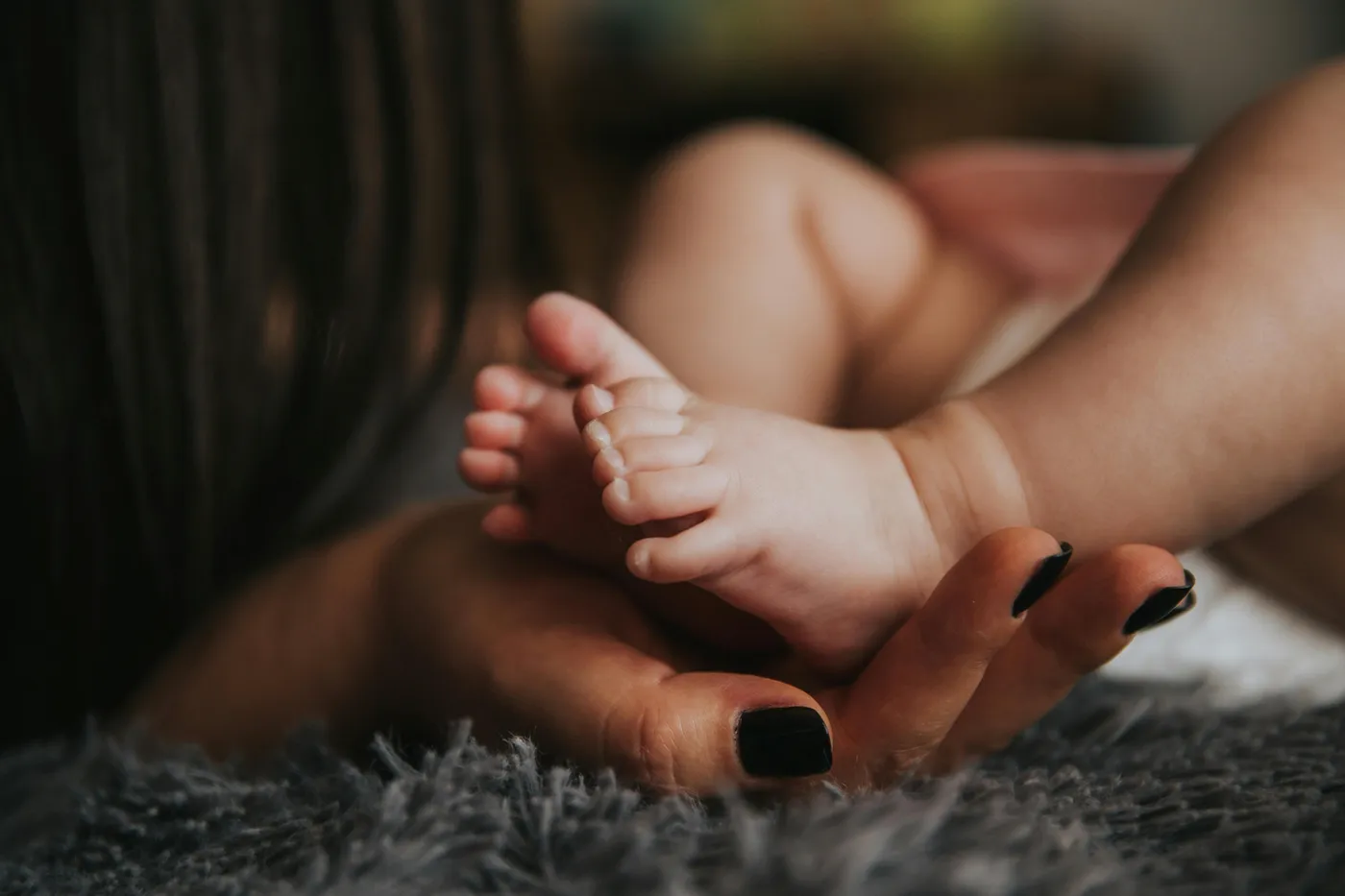 A mother gently holding her newborn baby’s feet
