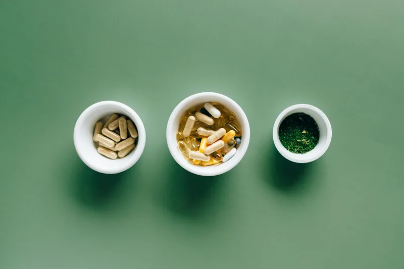 Three small bowls of capsules and herbs on a green background